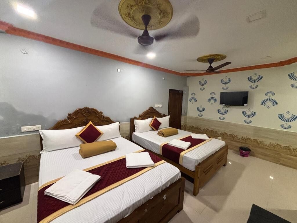 A hotel room with two beds, a ceiling fan, a television, and a decorative wall.