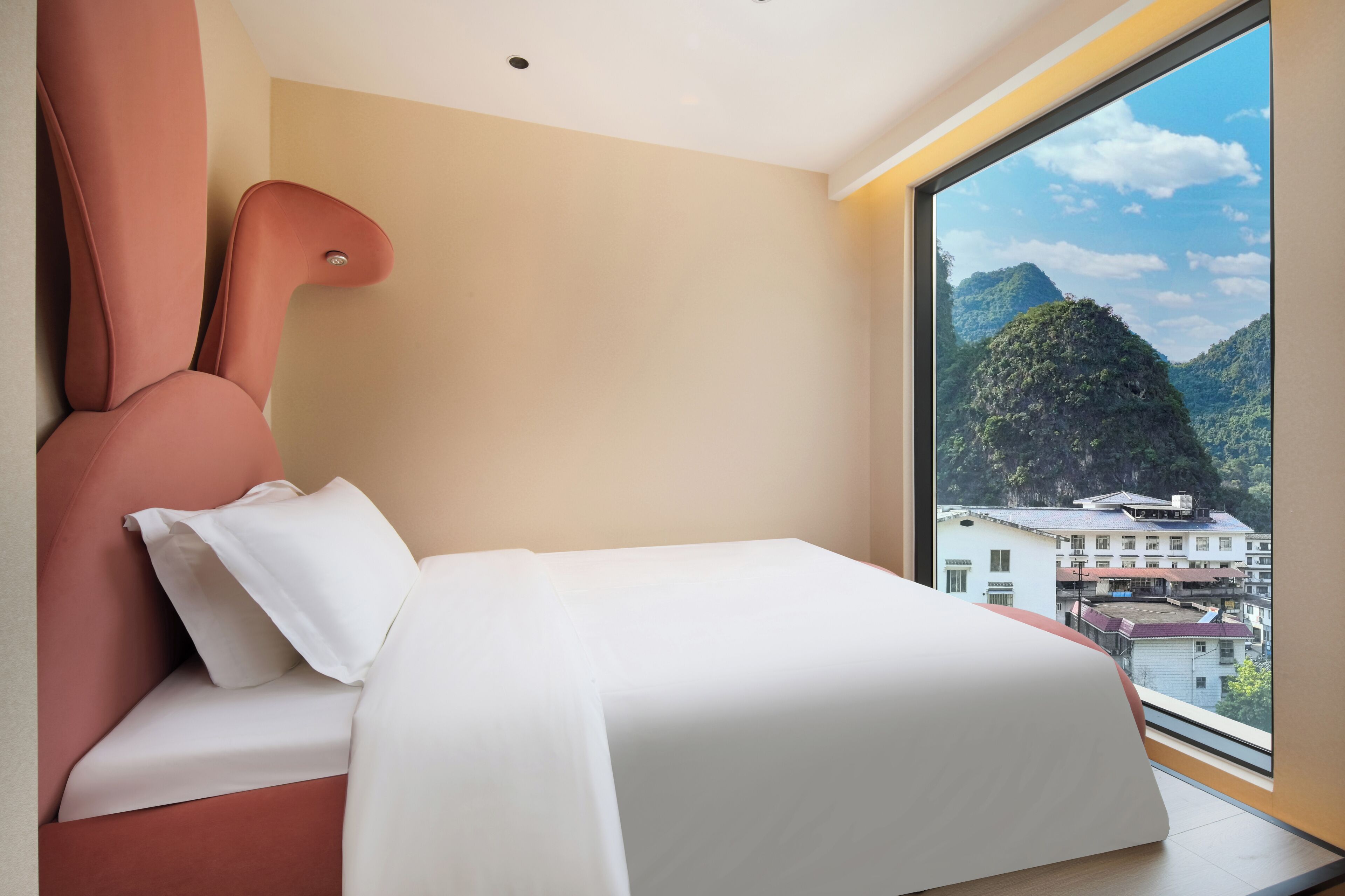 Habitación de hotel moderna con una cama grande, una silla roja llamativa y vistas a un paisaje montañoso a través de un ventanal amplio.
