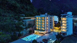 A modern hotel with multiple floors, a swimming pool, and a view of mountains. - Yun Pu Yun Shan Se Hotel (Guilin)