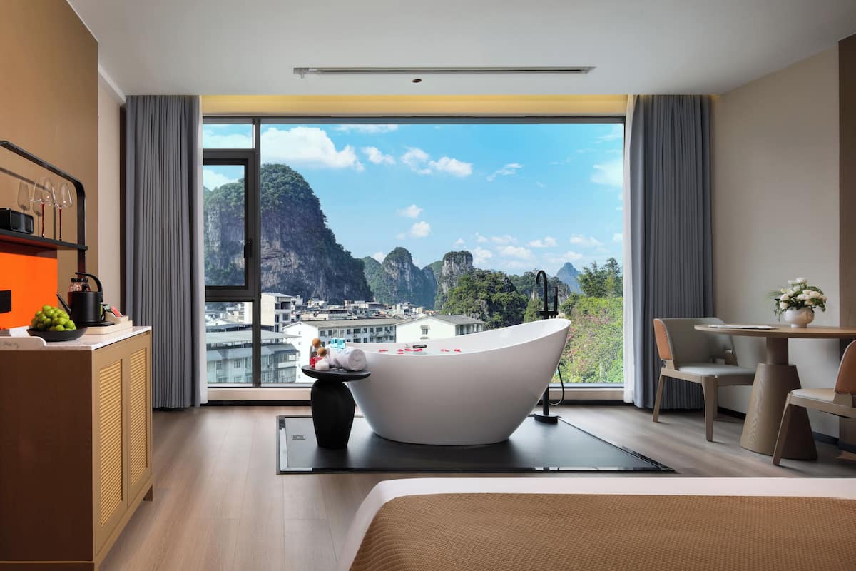 Ein modernes Hotelzimmer mit einer großen Badewanne, einer Essecke und Blick auf eine Berglandschaft.