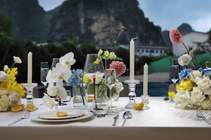 A table set with white flowers, candles, and glassware, with a mountainous backdrop. - Yun Pu Yun Shan Se Hotel (Guilin)