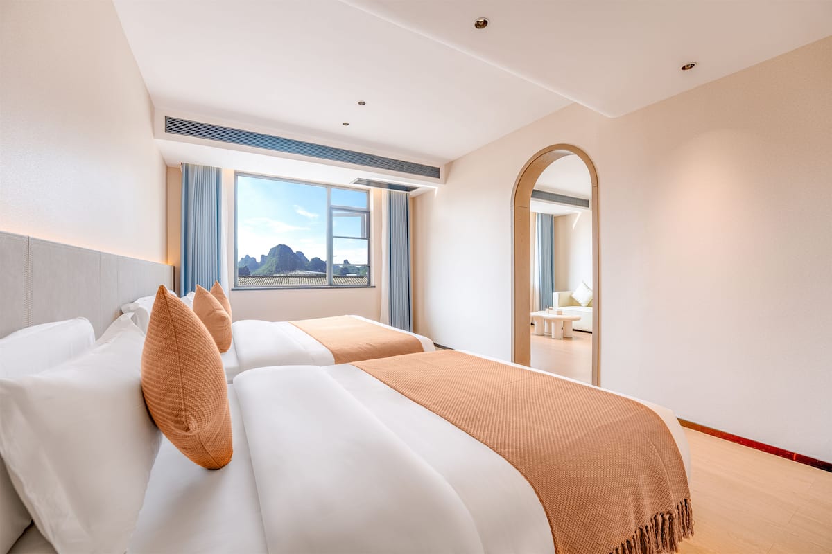 Ein Hotelzimmer mit zwei Betten, einem großen Fenster mit Blick, einem Spiegel und einem Deckenventil.