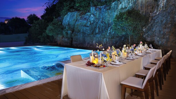 An outdoor dining area with a pool, tables set for a meal, and a rocky cliff backdrop. - Yun Pu Yun Shan Se Hotel (Guilin)