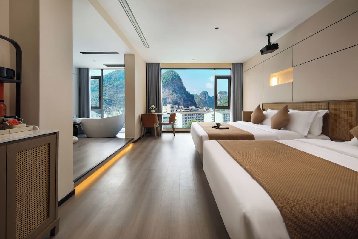 Ein Hotelzimmer mit zwei Betten, einem großen Fenster mit Stadtblick, einem Schreibtisch und einer Badewanne.