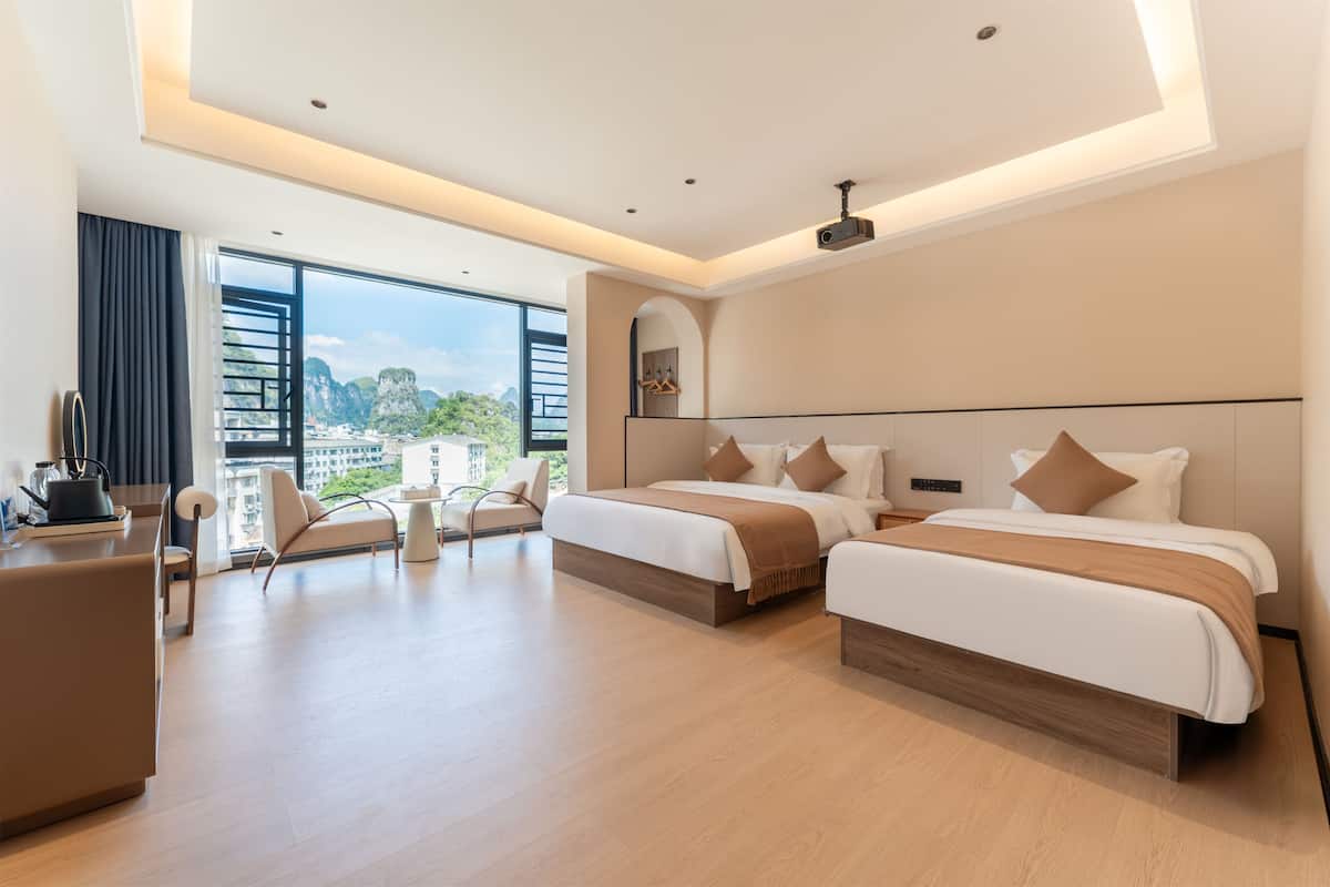 Ein modernes Hotelzimmer mit zwei Betten, einem Schreibtisch und Blick auf die Stadt.