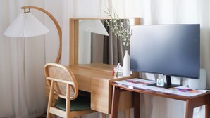 Hotellihuone, jossa on puinen työpöytä, televisio, tuoli, lamppu ja ruokapöytä, jonka päällä on kuppeja.