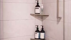 Suihkussa on käsisuihkupää ja seinään kiinnitetty hana. Siellä on myös kolme hyllyä, joilla on hygieniatuotteita.