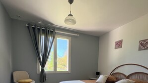 A bedroom with a bed, a chair, a desk, a window with curtains, and a ceiling fan.