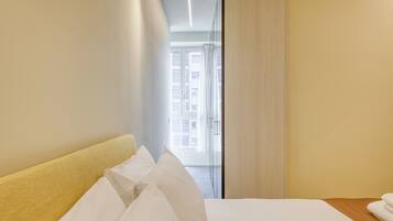 Habitación de hotel con cama, cabecera de madera, ventana con cortinas y vista a un edificio.