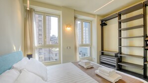 Hotellihuone, jossa on sänky, kaksi ikkunaa, sisäänrakennettu hylly ja näkymä kaupunkiin.