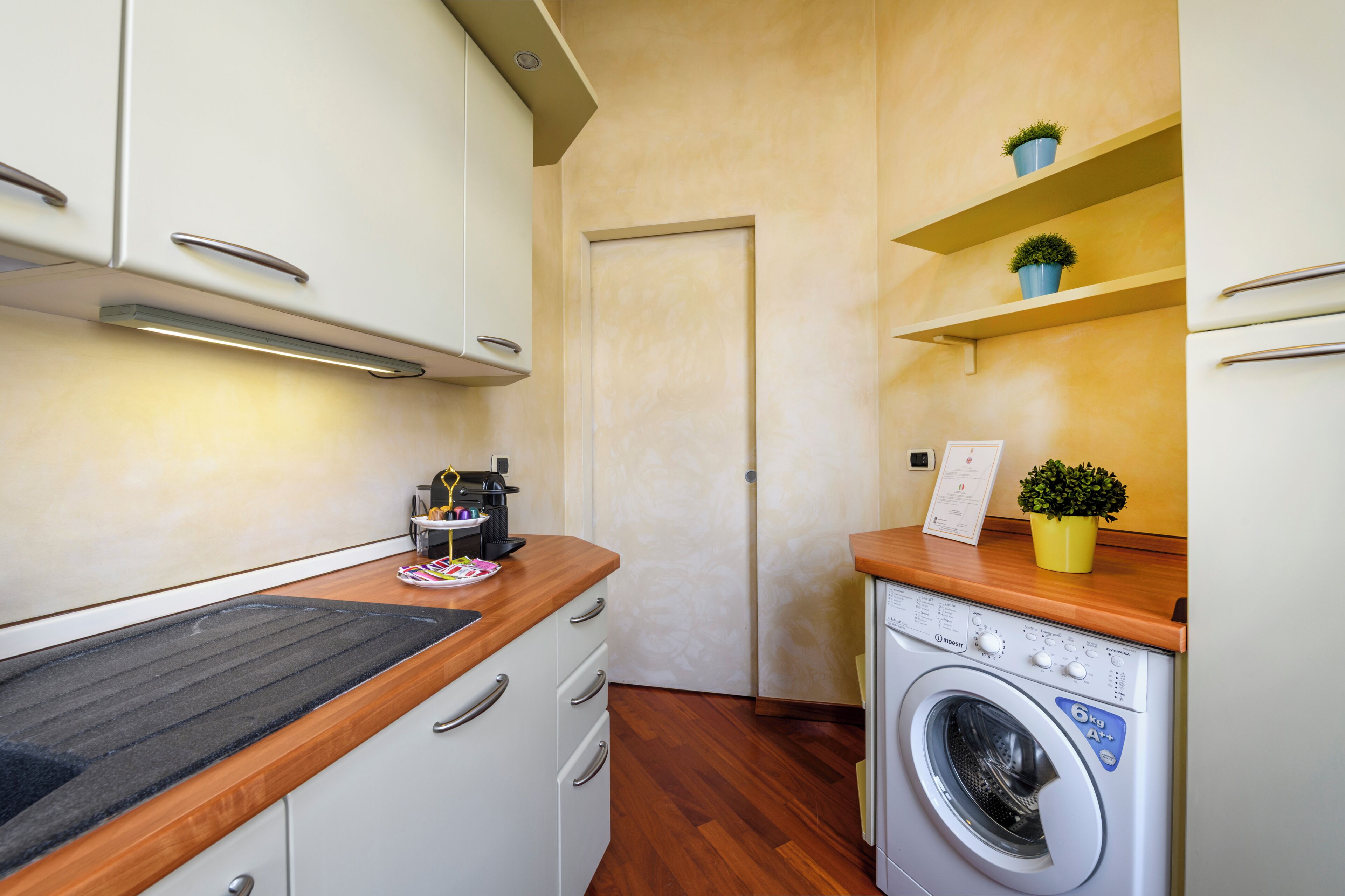 A compact kitchen with a washing machine, wooden countertop, and white cabinets.