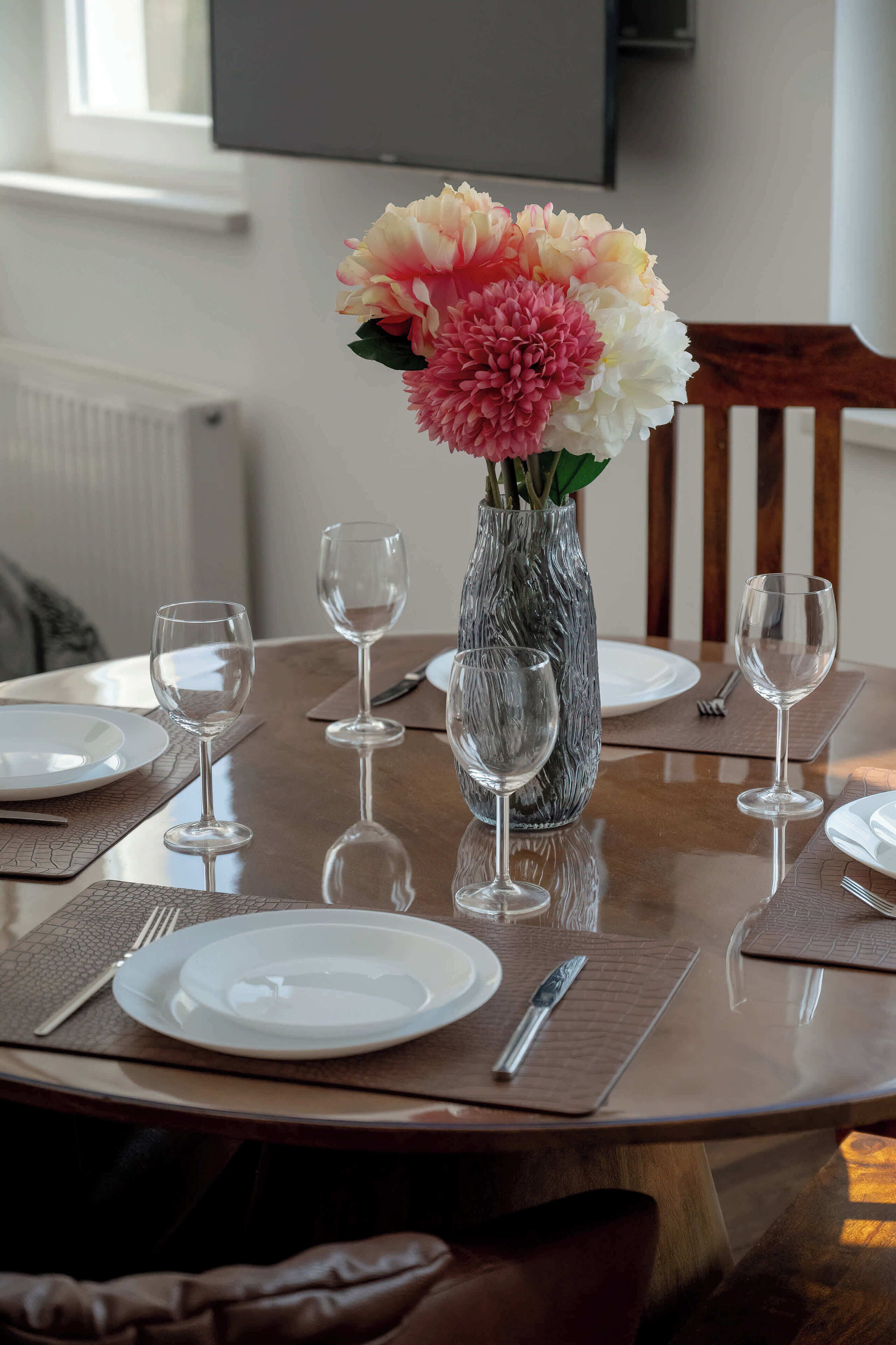 A dining table with a vase of flowers, empty wine glasses, plates, and cutlery.