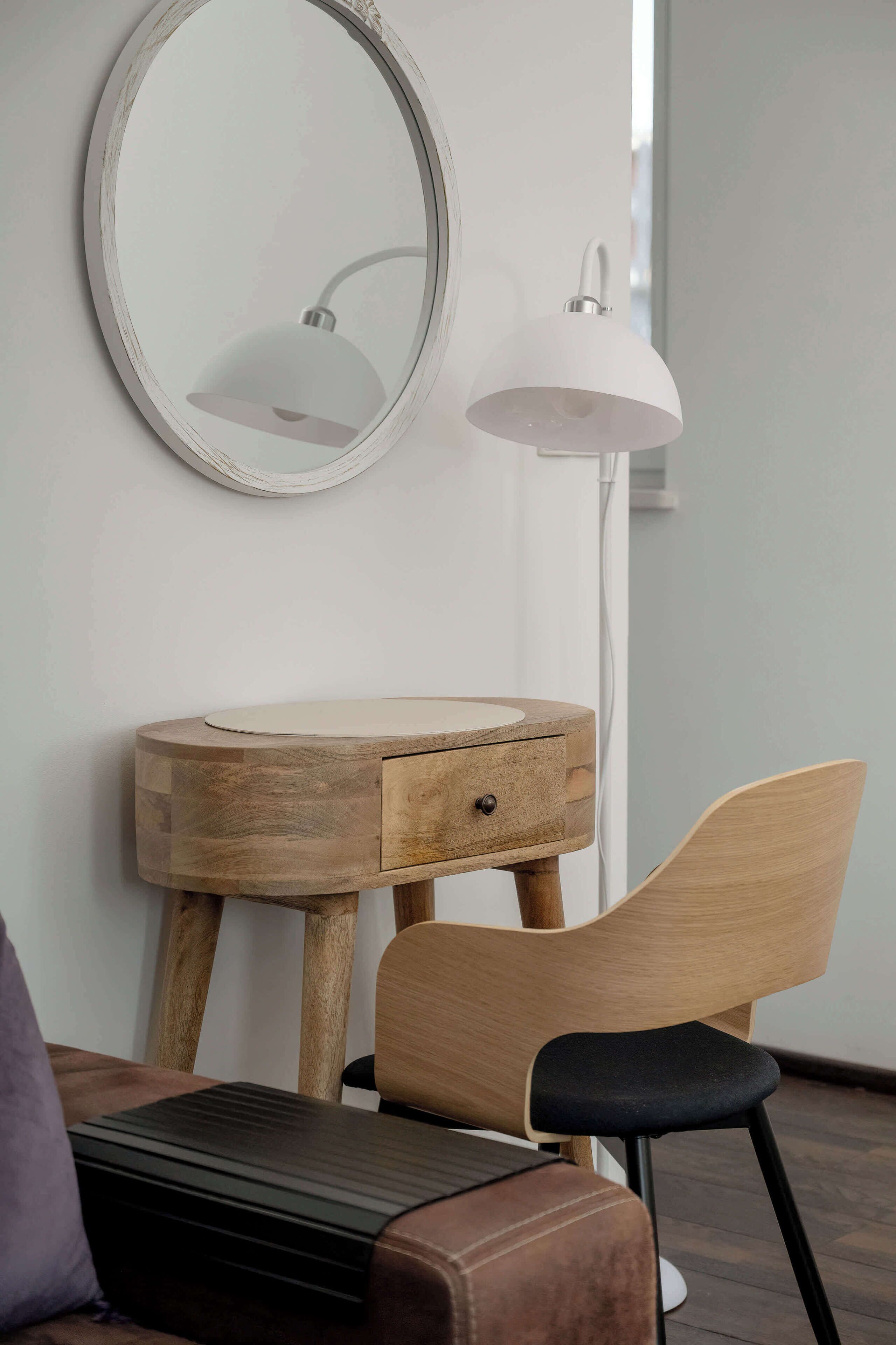 Ein hölzerner Waschtisch mit Spiegel und einer weißen Lampe, ein schwarzer Stuhl und eine braune Ledobank.