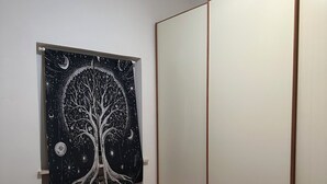 Een slaapkamer met een bed, een kledingkast en een wandtapijt met een ontwerp van een boom.
