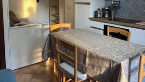 Een kleine keuken met witte kasten, een inbouwoven en een eethoekje met een tafel en stoelen.