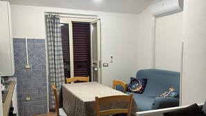 Een ruimtelijke woonkamer met een eettafel, stoelen, een bank, een kitchenette en een plafondventilator.