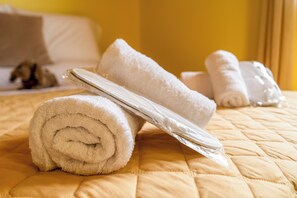 A bed with rolled white towels and a plastic bag on a quilted bedspread. - Amaryllis Haus (Zakynthos)