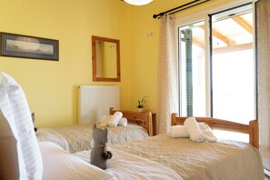 A hotel room with two beds, a wooden headboard, a mirror, a radiator, and a window with curtains. - Amaryllis Haus (Zakynthos)