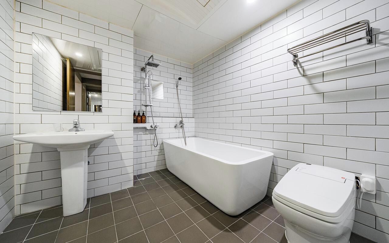 Un bagno moderno con piastrelle bianche a metro, una vasca freestanding, un lavabo su piedistallo e un water.