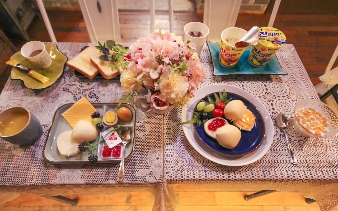 Une table dressée avec une variété d’aliments, notamment du pain, des fruits et des condiments, disposés sur une nappe en dentelle.