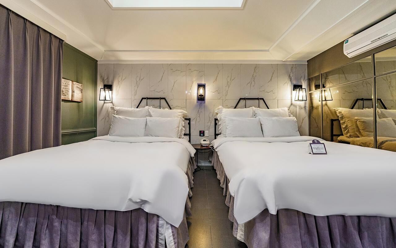 Habitación de hotel con dos camas, un espejo, tocador y tragaluz.