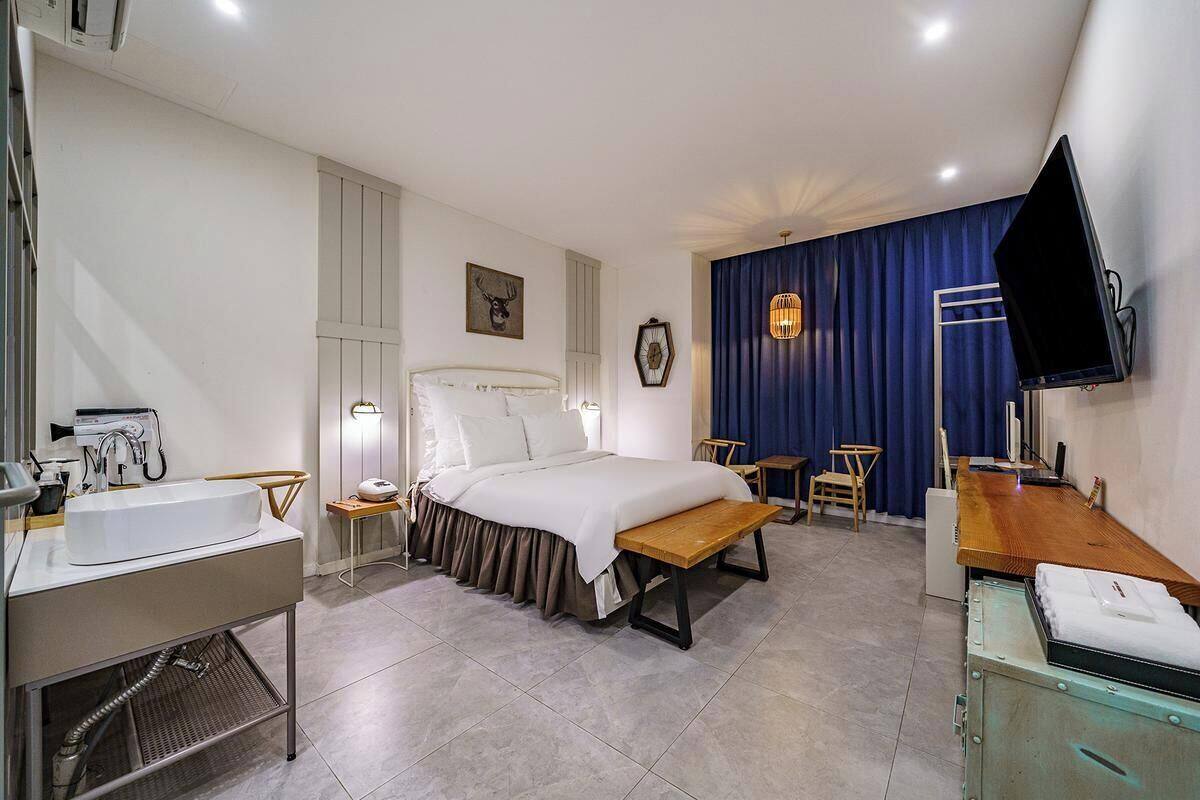 Una camera d'albergo con un letto, un comodino, una scrivania, una sedia e una TV montata a parete.