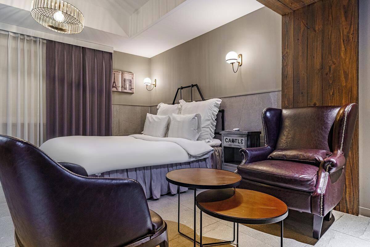 Camera d'albergo con un letto, due poltrone in pelle, un tavolino e un comodino con una lampada.