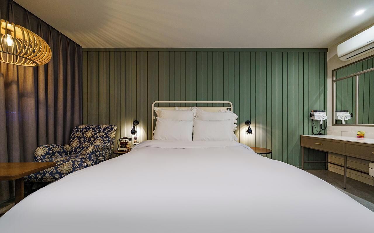Une chambre d’hôtel avec un grand lit, une chaise, des tables de chevet, un bureau et un appareil de climatisation.