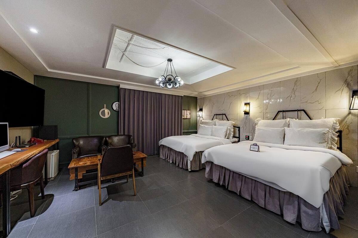 Camera d'albergo con scrivania, due letti, un lampadario e vista sulla città.