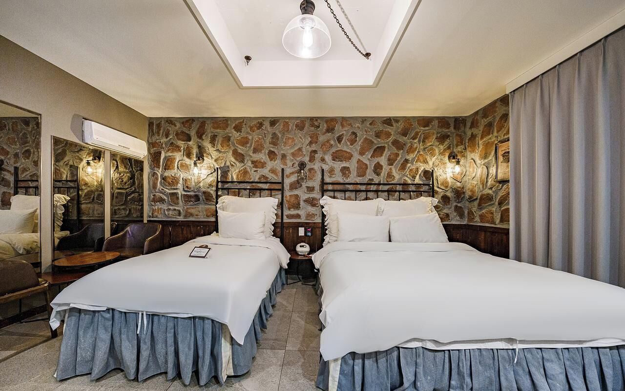 Un dormitorio con dos camas, decoración de pared de piedra, una lámpara en el techo y un espejo.