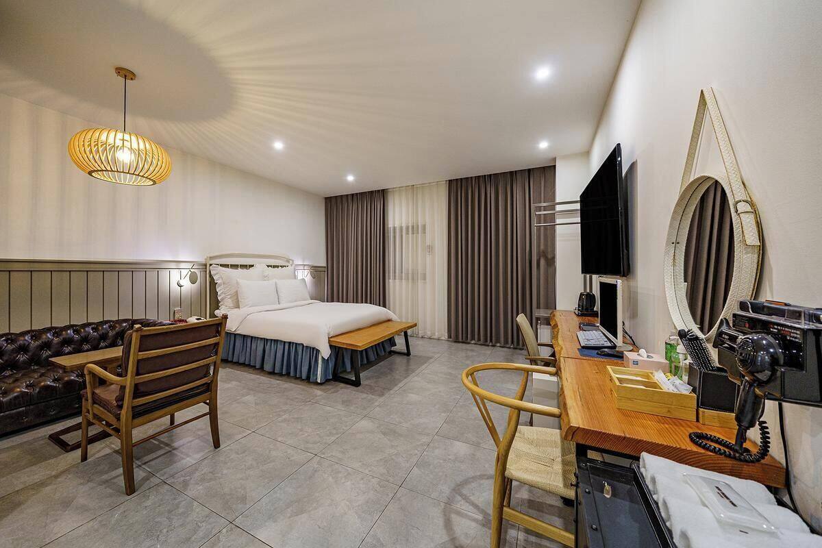 Camera d'albergo con un letto, una scrivania con il telefono, una sedia, un divano e uno specchio grande.