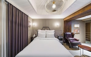 Ein Hotelzimmer mit einem Bett, einem Sessel, einem Schreibtisch, einer Lampe und einem Bücherregal.