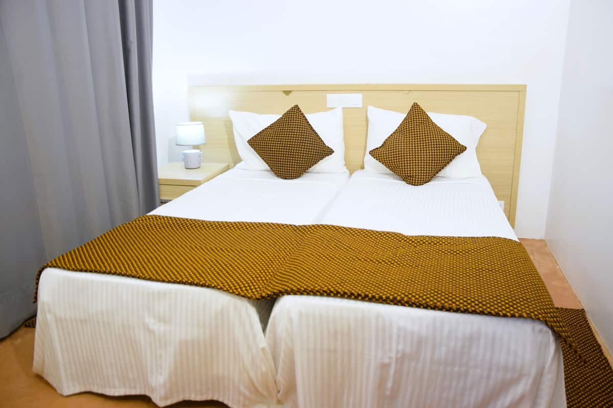Una cama doble con cabecera de madera, ropa de cama blanca y dos almohadas estampadas.