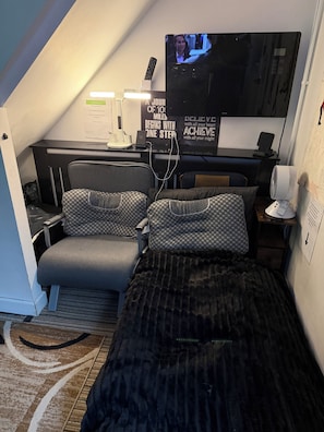 Une petite pièce comprenant un lit, un bureau avec un ordinateur, une télévision et une affiche motivante.