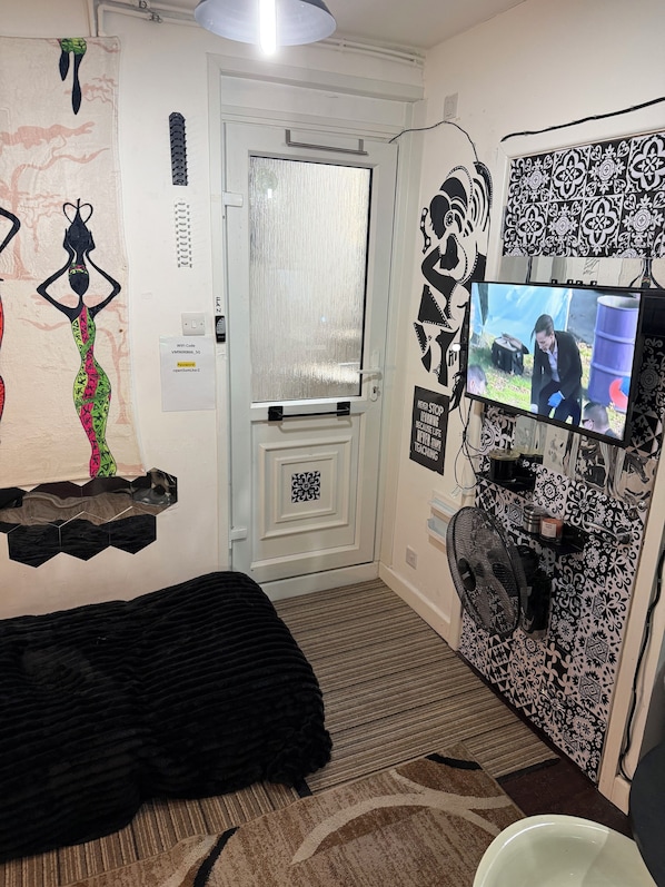 Une chambre comprenant un lit, un téléviseur fixé au mur, une porte avec une vitre en verre dépoli, et un mur orné de carreaux décoratifs et d’une affiche.
