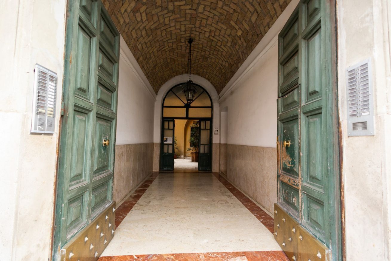 A corridor with green doors, a tiled floor, and a brick ceiling.