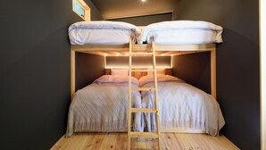 Een stapelbed met een houten trapje, een klein raam en een wandlamp.