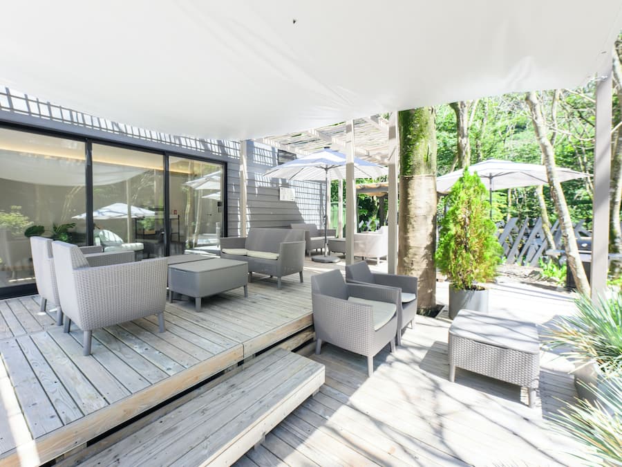 Alpendre coberto com móveis de vime, um deck de madeira e uma porta de vidro que dá para um jardim.