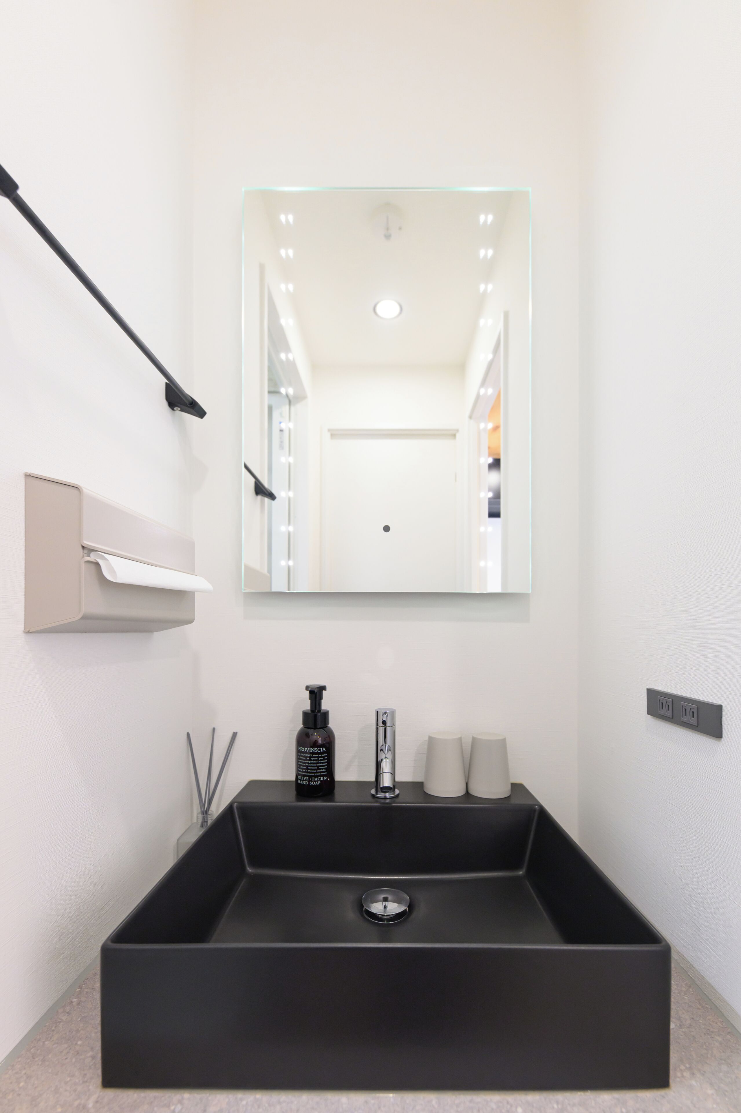 A modern bathroom with a large rectangular sink, a wall-mounted mirror, and a towel dispenser.