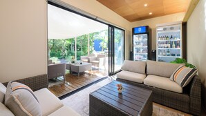A modern living room with a sofa, coffee table, and a glass door leading to a patio area. - THE GUEST VILLAGE Hakone Ashinoko (Hakone)