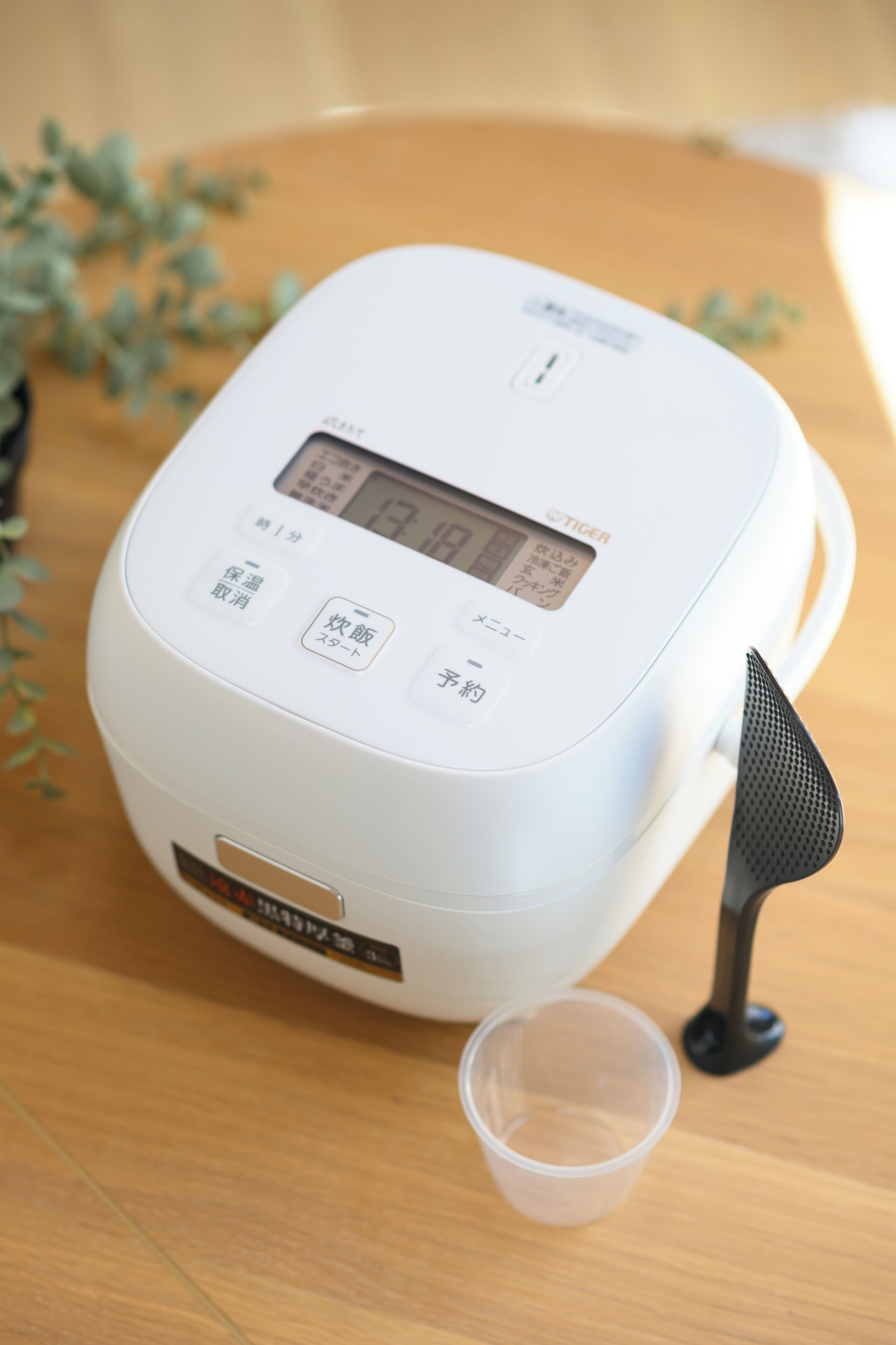 A rice cooker with a digital display, buttons, and a small cup beside it.