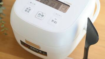 A rice cooker with a digital display, buttons, and a small cup beside it.