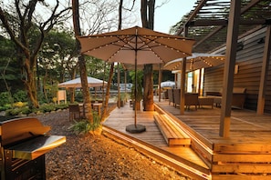 Une terrasse extérieure avec des bancs en bois, des parasols et un espace barbecue.