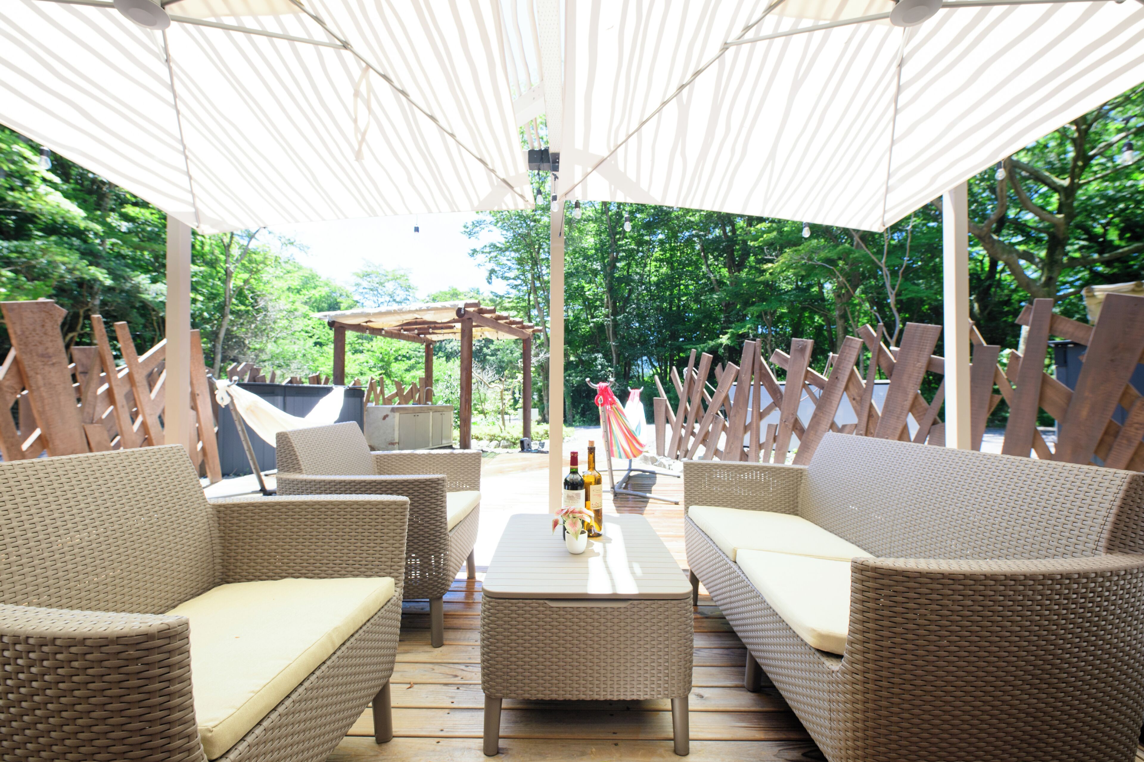 Un patio al aire libre con mobiliario de mimbre, una mesa con botellas y una hamaca.
