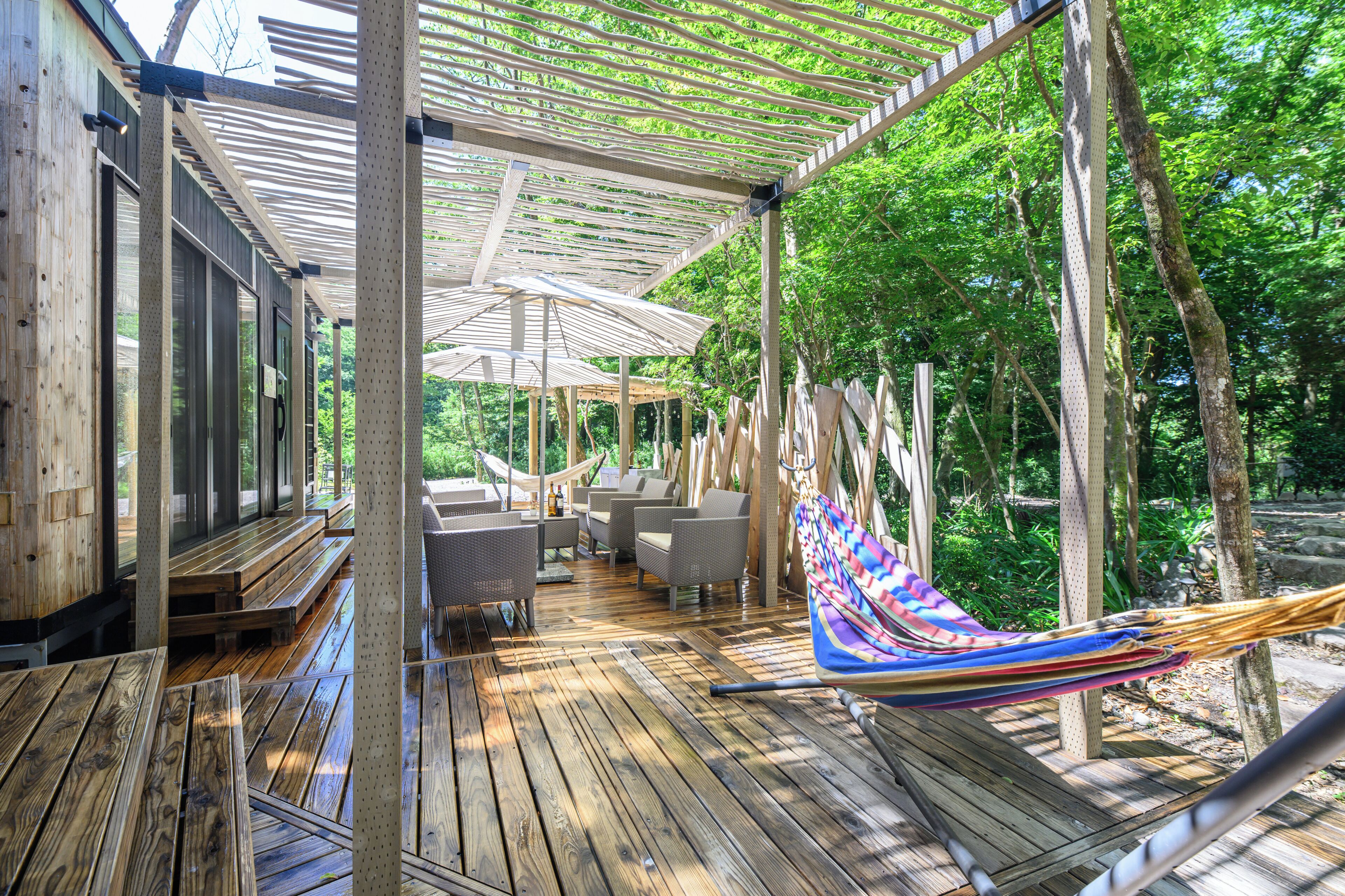 A wooden deck with outdoor furniture, a hammock, and a pergola structure.