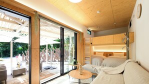 Een moderne kamer met een grote schuifglazen deur, houten plafond, een bank, een klein rond tafeltje en een bed.