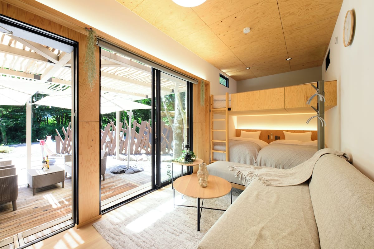 Une chambre moderne dotée d’une grande porte-fenêtre coulissante, d’un plafond en bois, d’un canapé, d’une petite table ronde et d’un lit.