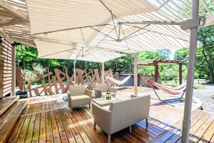 Una terraza de madera con mobiliario exterior, una hamaca y un pérgola con otra hamaca.