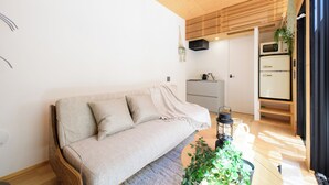 A modern living room with a sofa, a coffee table with plants, a clock on the wall, and a kitchen in the background. - THE GUEST VILLAGE Hakone Ashinoko (Hakone)
