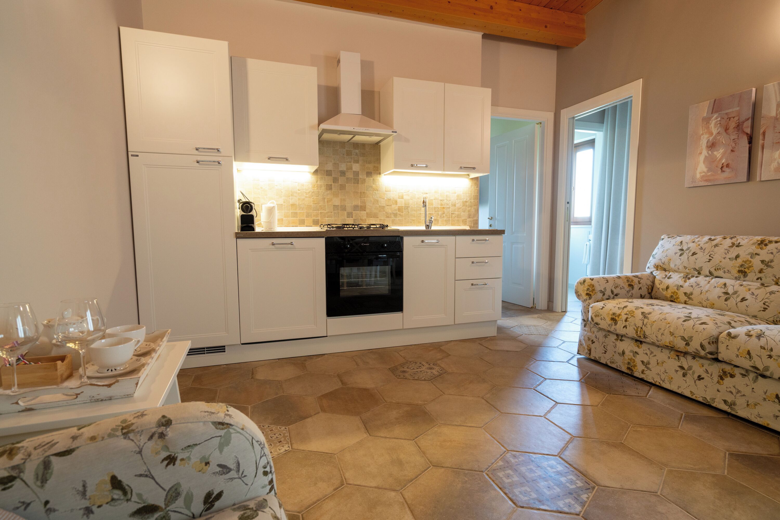 A kitchen with white cabinets, a tiled backsplash, and a dining area with a floral sofa and table set.